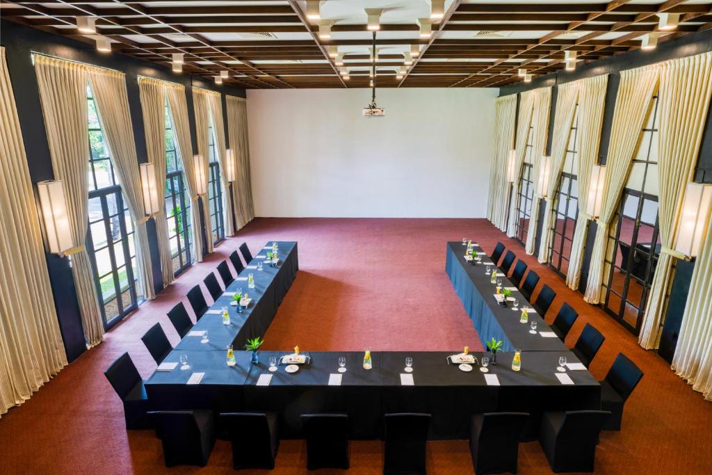 Konferenču zāle ar U formā novietotiem galdiem, elegantām melnām krēsliem un dekoratīvām detaļām, piemērota biznesa sanāksmēm. Gaismas un plašas logu ailes rada patīkamu atmosfēru.