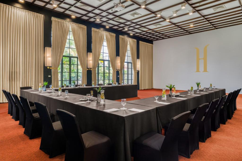 Konferenču telpa ar melniem galdiem un krēsliem, liela loga ar aizkariem un modernu apgaismojumu. Telpai ir eleganta atmosfēra un ir izveidota, lai veicinātu produktīvu sapulču norisi.