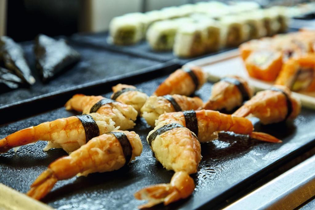 Garneles suši ar nori uz melnas plāksnes, fonā redzami dažādi suši veidi.