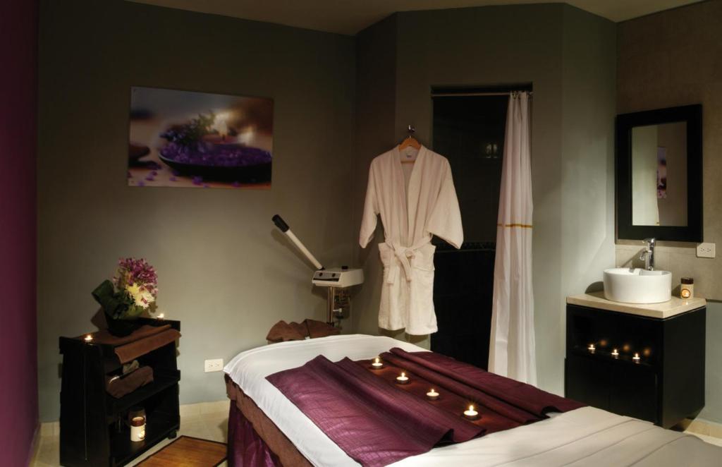 Relaksējoša spa telpa ar masāžas gultu, mīkstām dvieļiem un aromātiskām svecēm. Interjerā dominē siltas krāsas un relaksējoša atmosfēra.