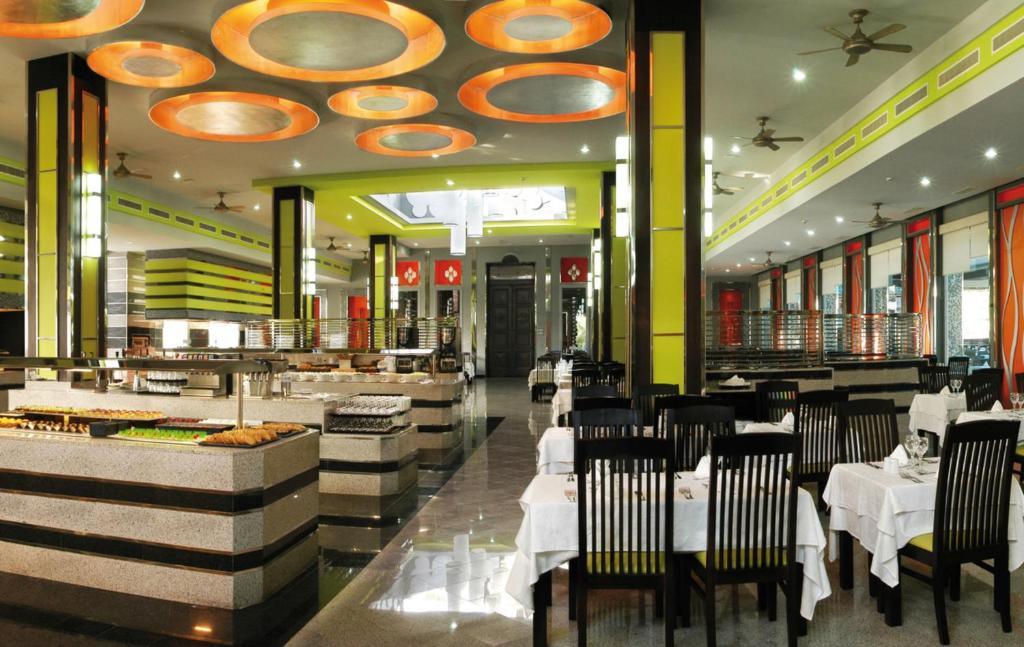 Moderns restorāns ar elegantām melnām mēbelēm un krāšņiem apgaismojuma elementiem, piedāvājot plašu ēdienu izvēli un viesmīlīgu atmosfēru.