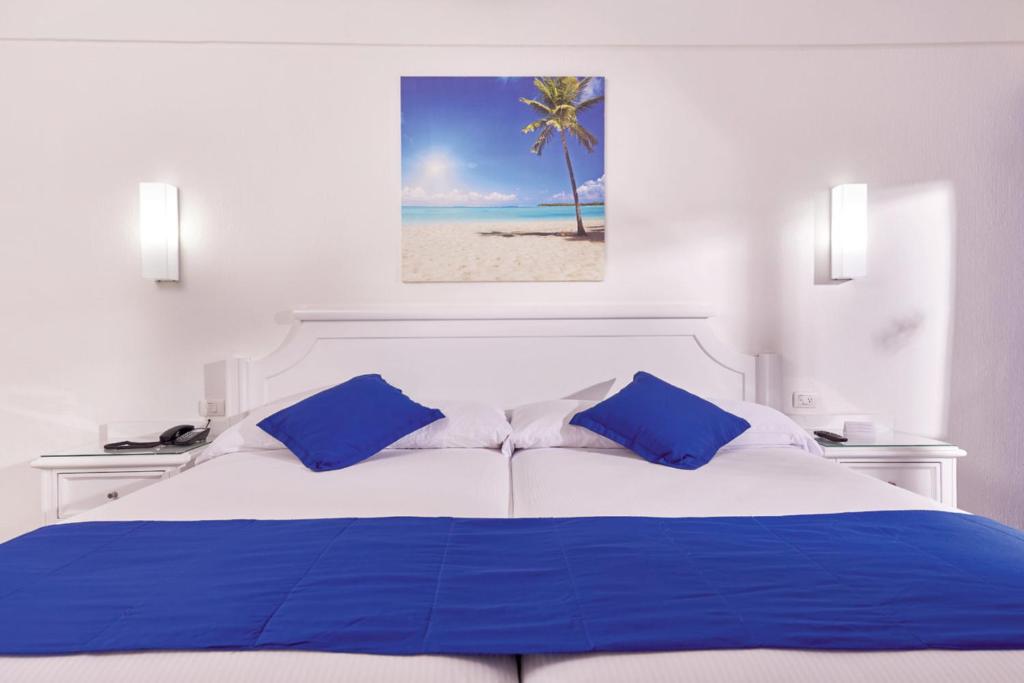 Mūsdienīgs viesnīcas numurs ar divām gultām un zilu dekori, piesaistoša ainava ar palmu uz sienas. Ideāls relaksācijai un atpūtai.