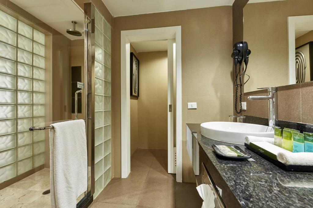 Moderns vannas istabas interjers ar stikla sienām, melnu akmens izlietni un higiēnas piederumiem. Svaiga un eleganta atmosfēra.