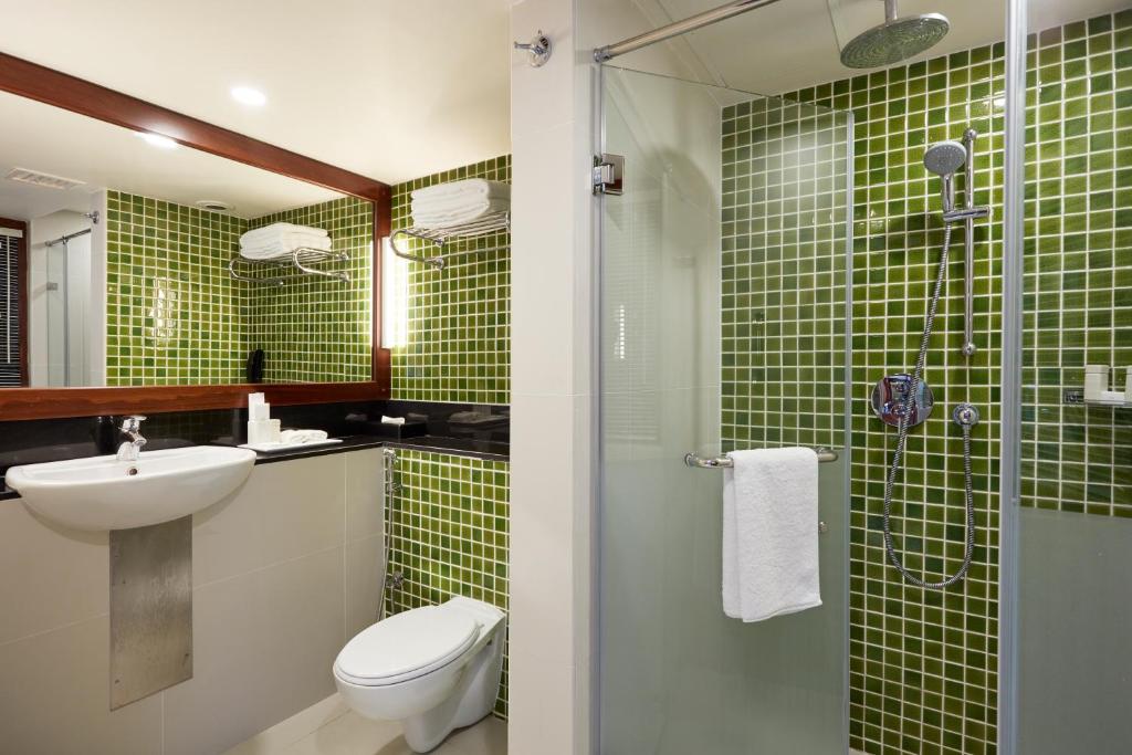 Mūsdienīgs vannas istabas interjers ar zaļiem mozaīkas flīzēm, peldošu izlietni un dušas kabīni. Ērti uzglabāšanas risinājumi un gaismas apgaismojums rada patīkamu atmosfēru.