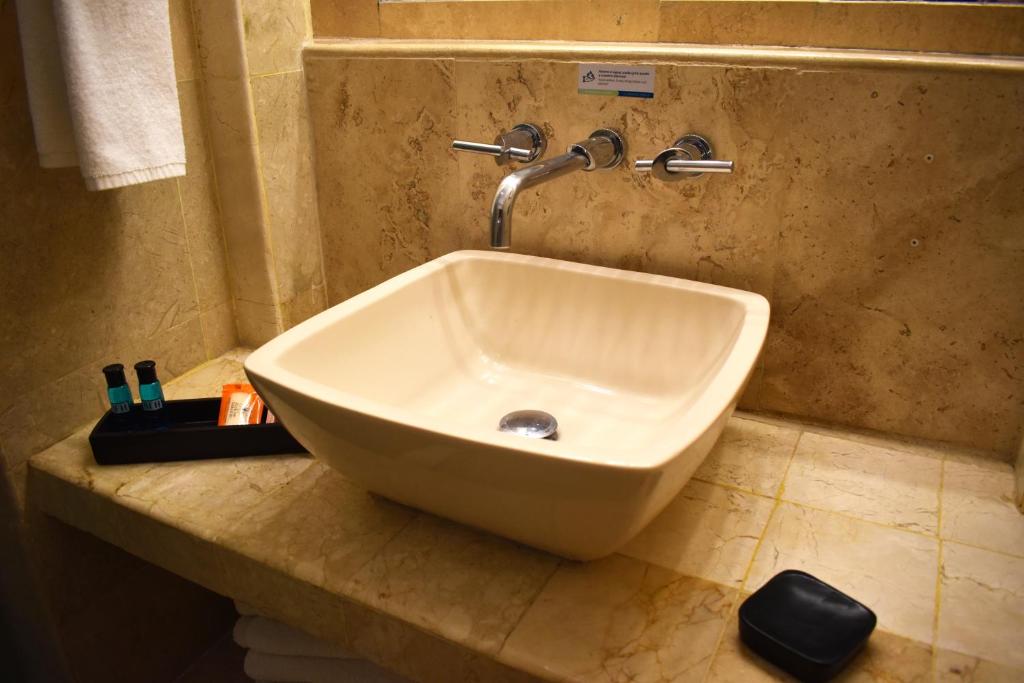 Mūsdienīgs vannas istabas izlietne ar elegantu kvadrātveida dizainu, kas novietota uz akmens virsmas. Blakus atrodas higiēnas piederumi un dvielis.