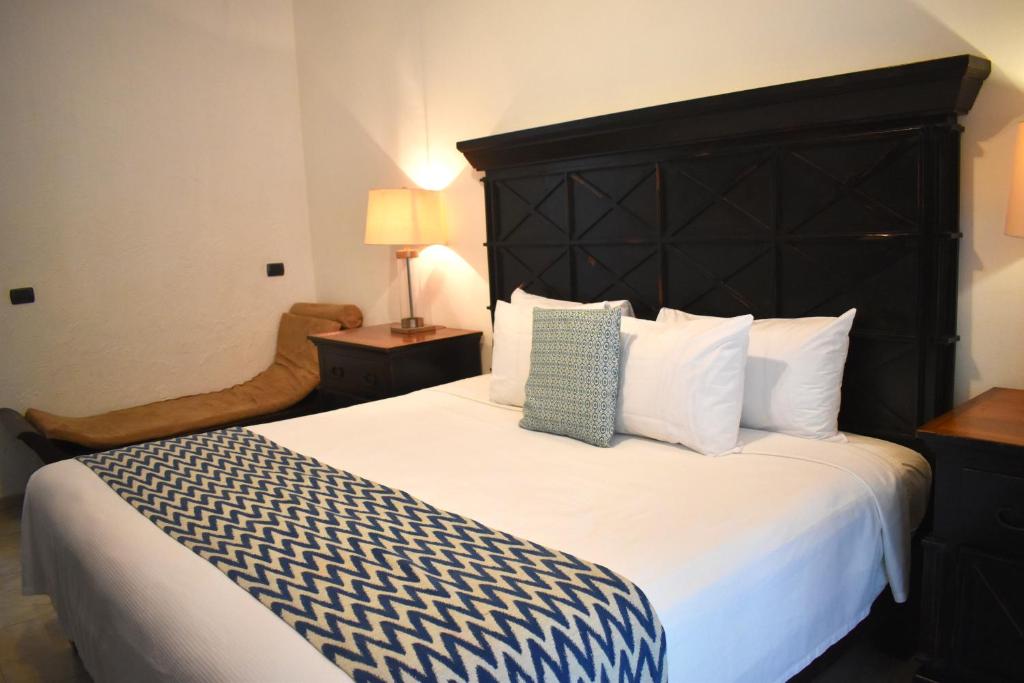 Mūsdienīgs guļamistabas interjers ar melnu gultas galvu, baltu gultu un zilu rakstu segu. Blakus ir ērta dīvāna tipa sēdeklis un naktsgaldiņš ar lampu.