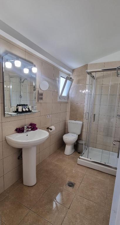 Mūsdienīgs vannas istabas interjers ar dušu, tualeti un izlietni, kas aprīkota ar spoguli un gaismekļiem. Svaigi ziedi pie izlietnes piešķir telpai patīkamu atmosfēru.