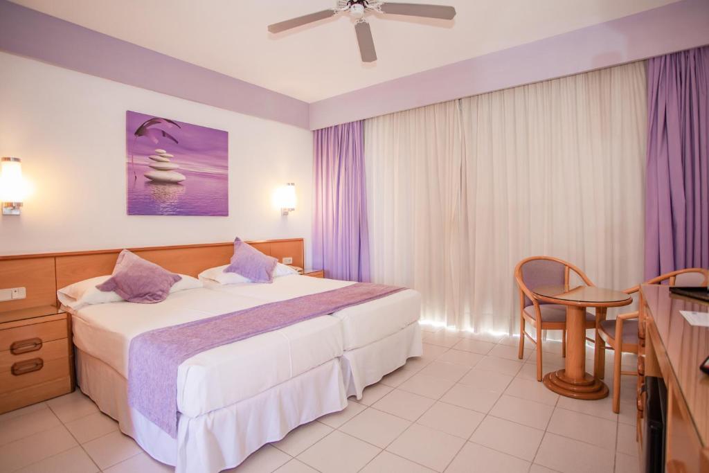 Mūsdienīga viesnīcas numura interjers ar divām gultām, purpura toņu akcentiem un koka mēbelēm, kas radījuši relaksējošu atmosfēru. Uz sienas redzama mākslas glezna ar purpura un baltajiem toņiem.