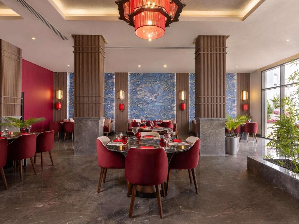 Mūsdienīgs restorāna interjers ar sarkaniem krēsliem un elegantām detaļām, uzsverot zilu tapeti ar ziedu motīviem. Atmosfēra ir stilīga un aicinoša, ideāli piemērota gardām maltītēm.