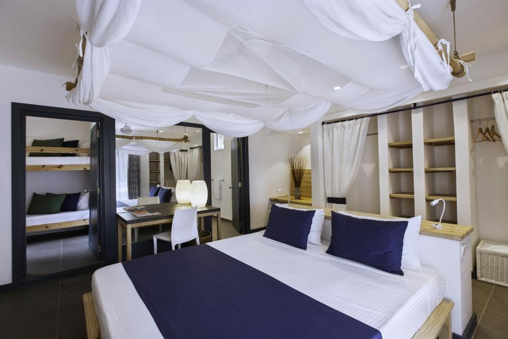 Moderns guļamistabas interjers ar baltu drānu piekārtu pie griestiem, divguļamā gulta un bunkuru gulta. Telpa ir gaiša un minimālistiska ar koka elementiem un ērtu rakstāmo.