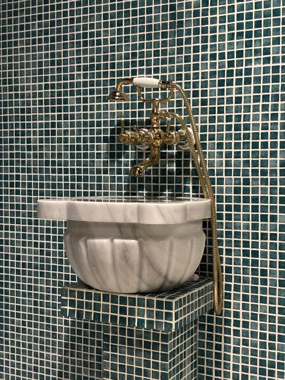 Marmora izlietne ar zelta krāsu jaucējkrānu, kas novietota uz mozaīkas flīžu fona.