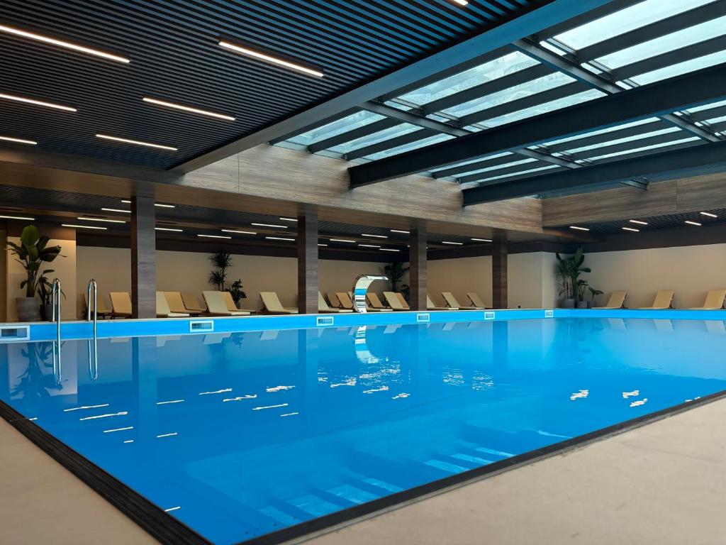 Mūsdienīgs iekštelpu baseins ar skaidru, zilu ūdeni un modernu apgaismojumu. Apkārt baseinam ir ērtas sauļošanās krēsli un zaļumi, kas piešķir telpai relaksējošu atmosfēru.