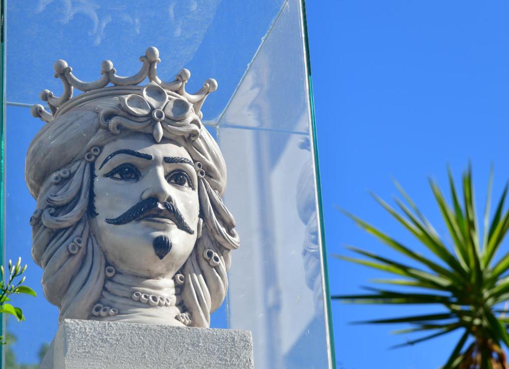 Aizraujoša keramikas skulptūra, kas attēlo vīrieti ar kroņu un ūsām, atrodas stikla vitrīnā zem skaidras debess. Skulptūra ir izsmalcināta un izceļas ar detalizētu sejas izteiksmi.