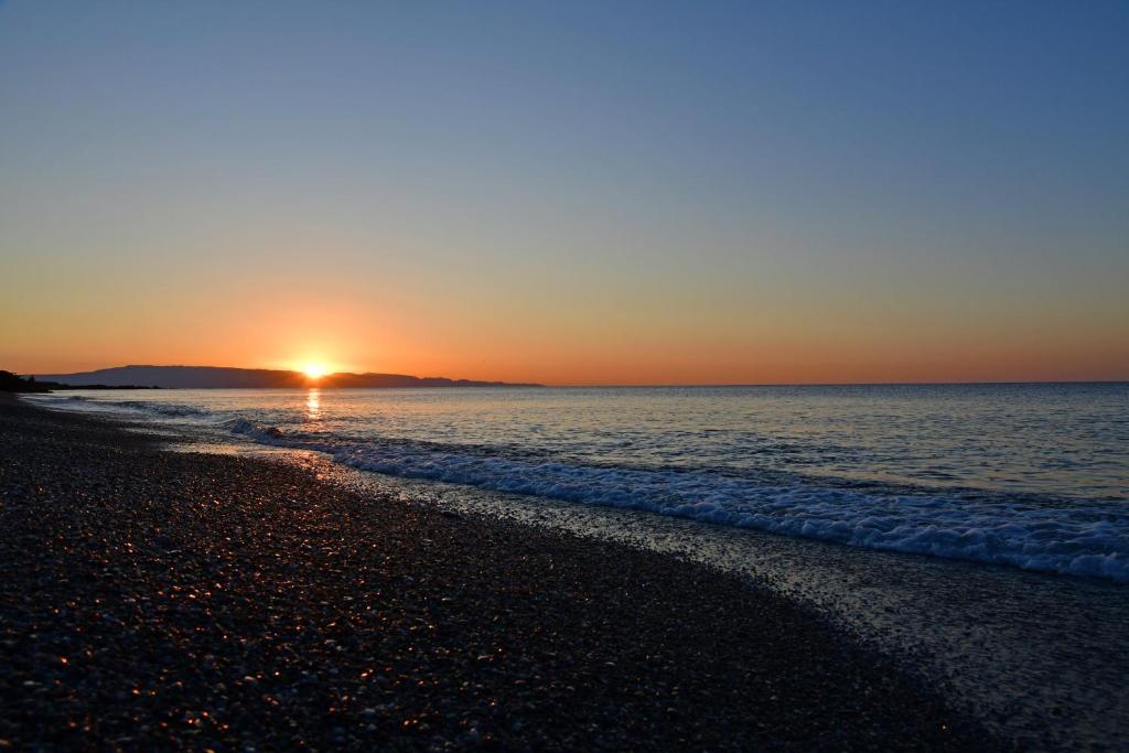 Saulriets pār mierīgu pludmali ar smiltīm un viļņu viļņiem, radot mierīgu un relaksējošu atmosfēru. Siltas krāsas piepilda debesis, veidojot skaistu ainavu.