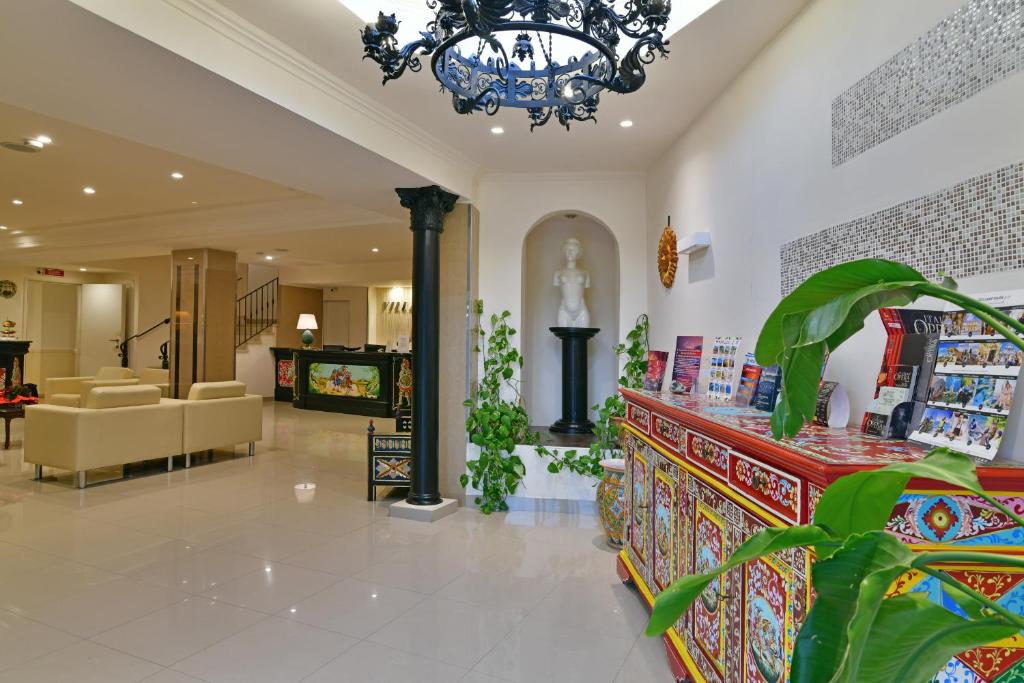 Mūsdienīgs viesnīcas vestibils ar elegantu apdari, dekoratīvu mēbeļu un augu klātbūtni, kas rada siltu un viesmīlīgu atmosfēru. Redzams arī statuja un informācijas stends ar brošūrām.