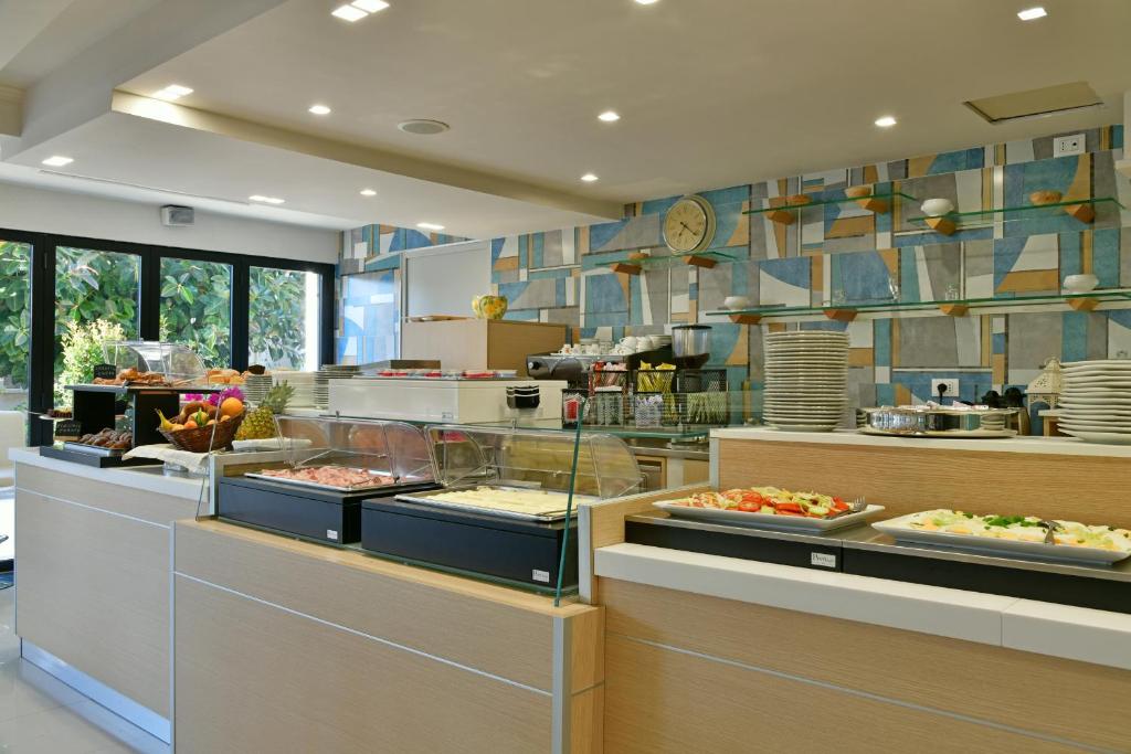 Mūsdienīga viesnīcas brokastu bufete ar dažādām ēdienu izvēlēm, tostarp augļiem un salātiem, gaišā un gaumīgā interjerā.