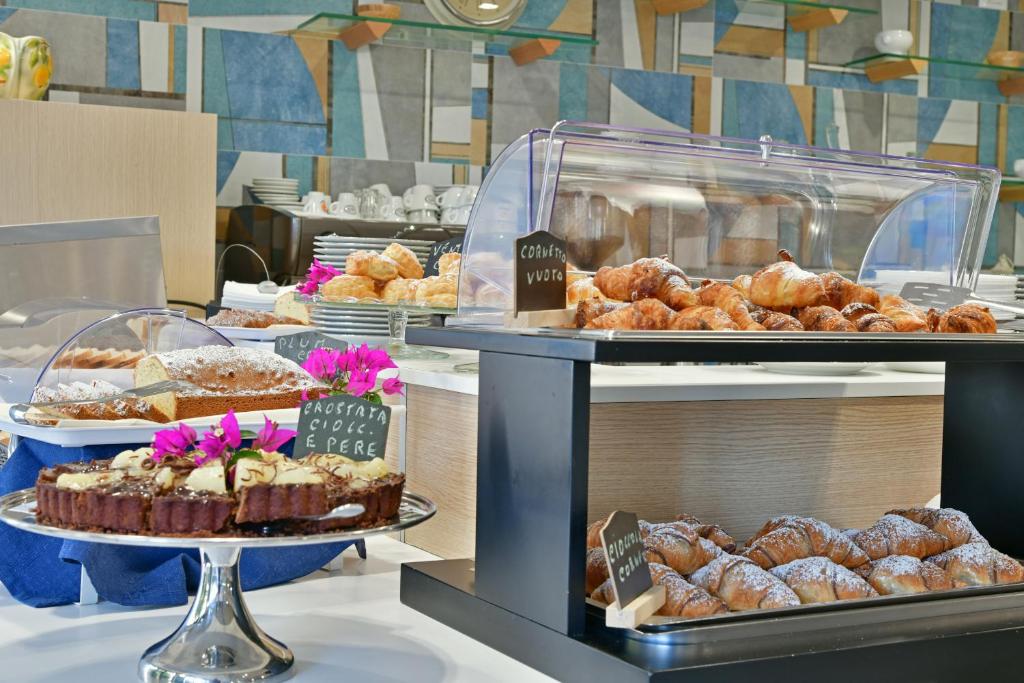 Bufete ar dažādiem konditorejas izstrādājumiem, tostarp kūkām un kruasāniem, dekorēta ar ziediem. Ideāla izvēle brokastīm vai desertiem.