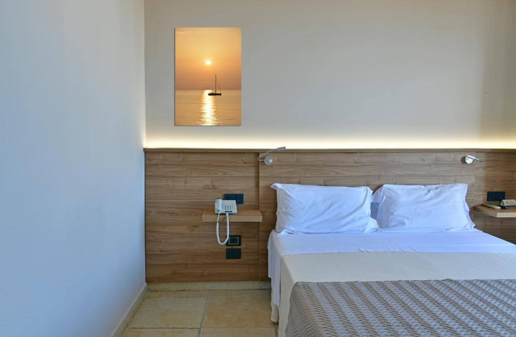 Mūsdienīgs guļamistabas interjers ar vienkāršiem koka elementiem, baltām gultas veļām un saulrieta ainavu uz sienas. Guļamistabā ir arī telefons un naktsgaldiņš.