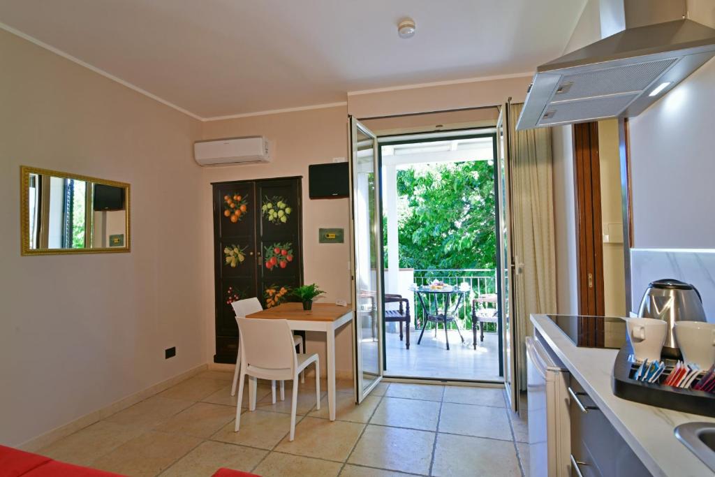 Moderns dzīvoklis ar atvērtu terasi, galds un krēsli, virtuve ar kafijas komplektu un augļu rotājumu skapī. Dabas skats pa durvīm.