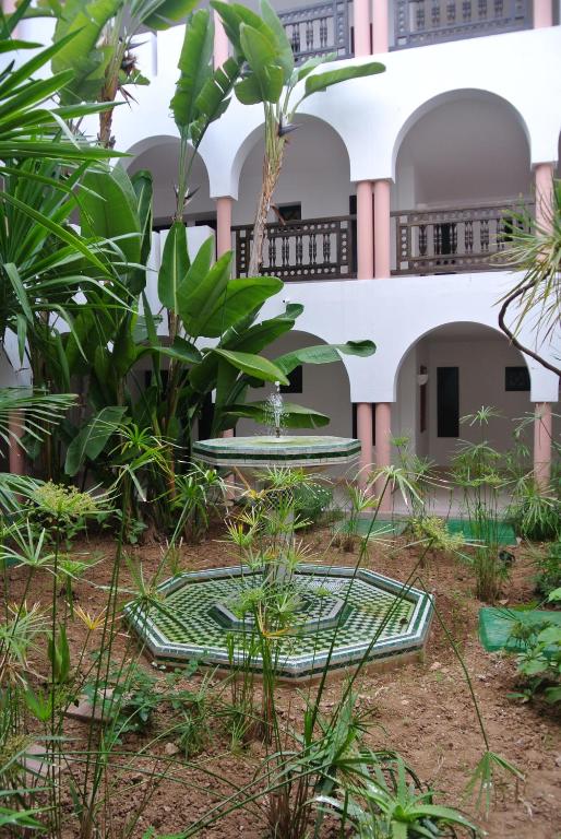 Skaists iekšpagalms ar strūklaku un zaļām augu kompozīcijām, kas veido mierīgu atmosfēru. Labi redzamas arkas un balkoni pie ēkas sienām.