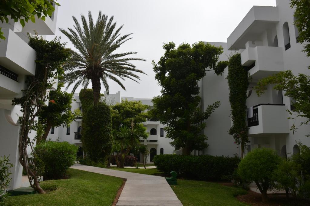 Zaļš, miera pilns dzīvojamais komplekss ar baltām ēkām un palmu kokiem, apzaļumots ar krūmiem un zāli. Ceļš ved cauri ainavai, radot relaksējošu atmosfēru.