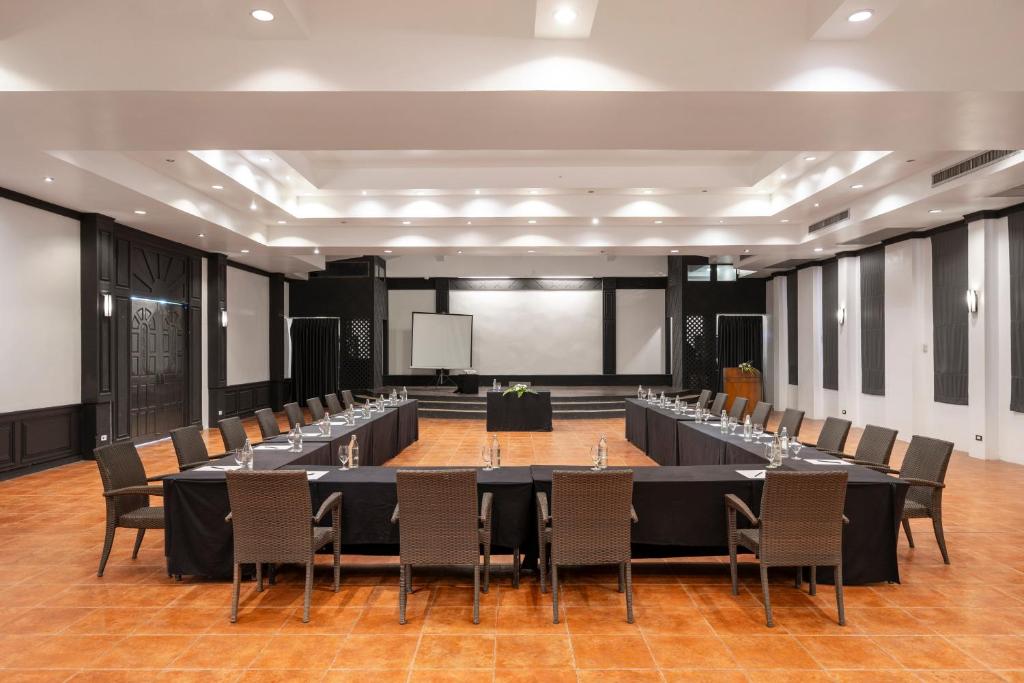 Konferenču telpa ar L formas galdu, ap kuru izvietotas ērtas krēsli. Telpa ir gaiša, ar modernu apgaismojumu un melnbaltām sienām, kas rada profesionālu atmosfēru.