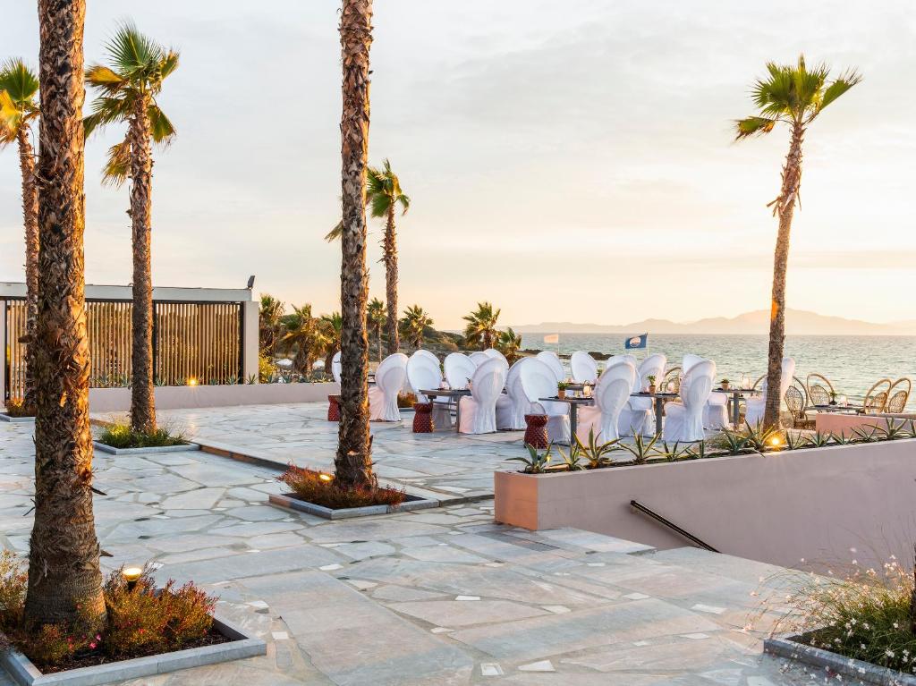 Lieliska pludmales kāzu vieta ar baltiem galdiem un krēsliem, palmām un gleznainu jūras skatu. Ideāla atmosfēra romantiskām svinībām saulrietā.