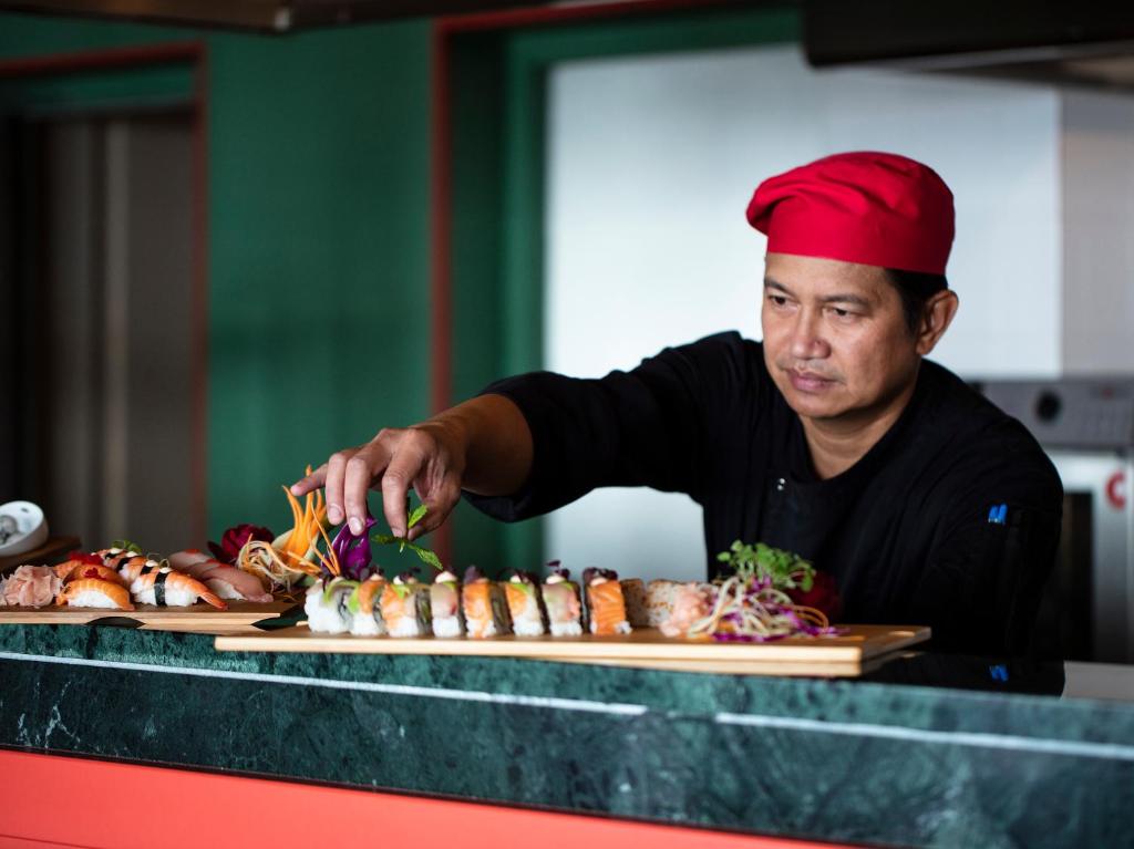 Sushi šefpavārs rūpīgi dekorē ēdienu, izmantojot svaigus dārzeņus un krāsainas sastāvdaļas. Fons ir mūsdienīgs un elegantā krāsā.