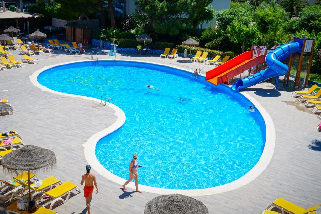 Peldbaseins ar zilu ūdeni un sarkanu ūdens slidkalniņu apkārtējos saulē atpūtas krēslos. Ideāla vieta atpūtai un izklaidei.
