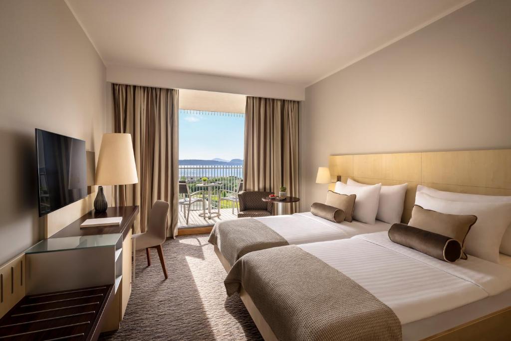 Mūsdienīgs viesnīcas numurs ar divām atsevišķām gultām, televizoru, un balkonu ar skatu uz ainavu. Interjers ir gaišs un elegants, nodrošinot komfortablu atmosfēru.