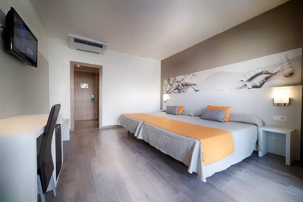 Mūsdienīga viesnīcas numura interjers ar diviem gultām, rakstāmgaldu un televizoru. Uz sienas ir smilšu un jūras gliemežvāku attēls, radot relaksējošu atmosfēru.