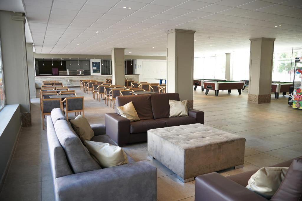 Mūsdienīgs un plašs atpūtas telpas interjers ar ērtām dīvānu grupām un koka galdiem, ideāli piemērots sociālai mijiedarbībai un atpūtai.