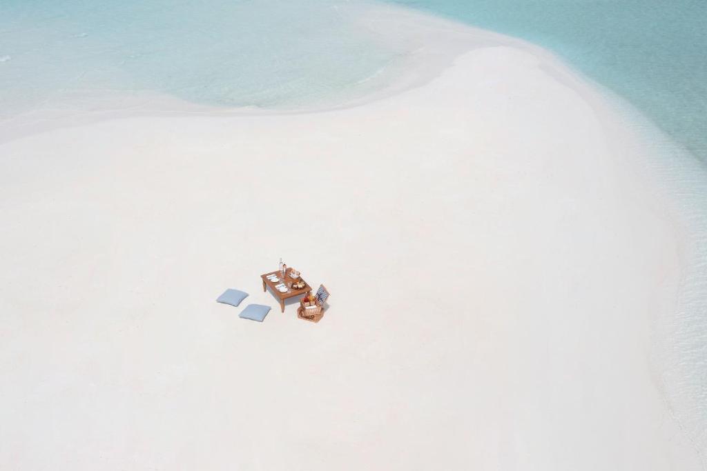Tuksnesīgs balts pludmales smilšu gabals ar ērtu galdu un krēsliem, ideāli piemērots relaksācijai un romantiskām maltītēm pie jūras.