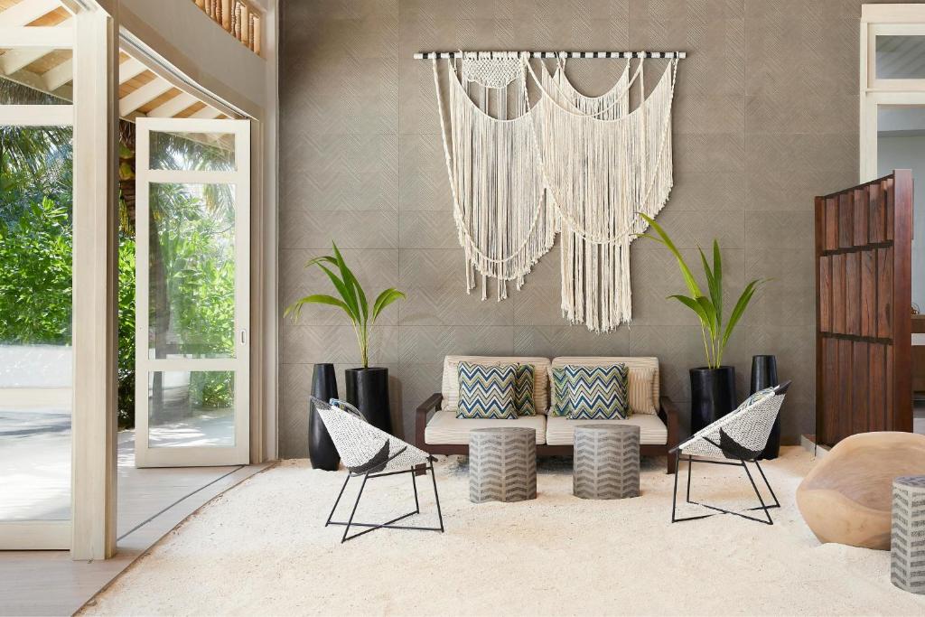 Mūsdienīgs viesistabas interjers ar makramē sienas dekoru, ērtiem krēsliem un augu akcentiem. Telpa ir gaiša un atvērta, radot relaksējošu atmosfēru.