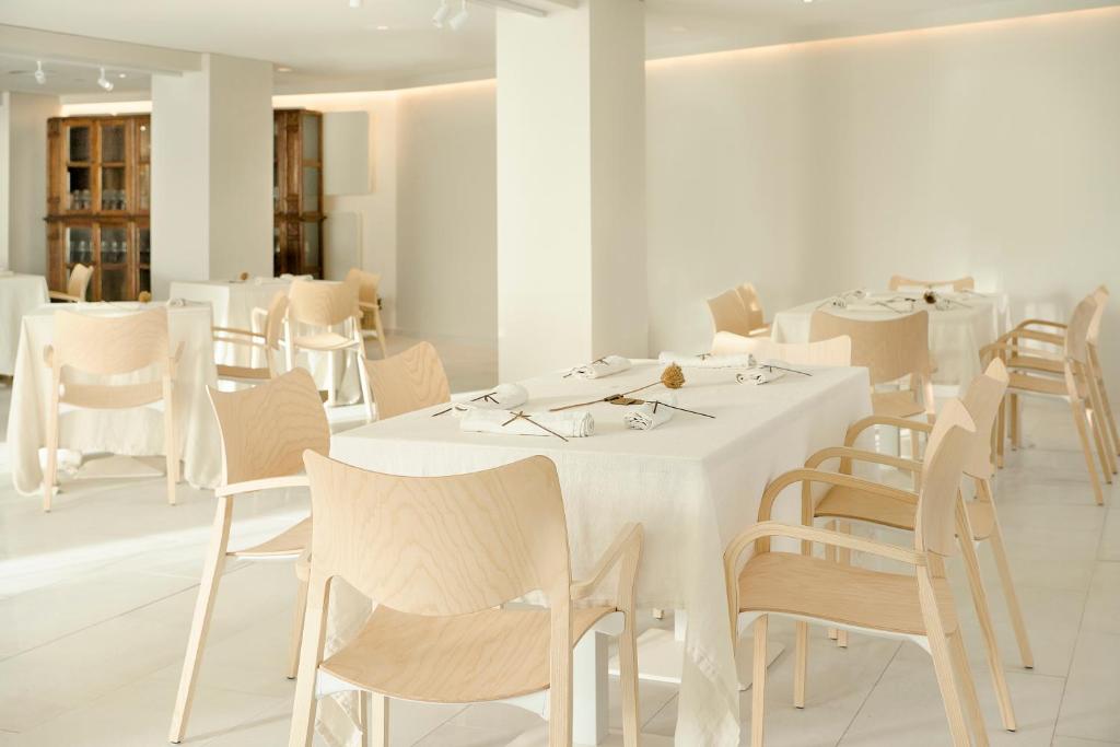 Mūsdienīgs restorāns ar gaišu interjeru, kas ietver koka galdus un krēslus. Uz galdiem ir klātas baltas galdautas un dekoratīvi elementi.