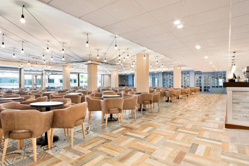 Mūsdienīgs restorāns ar plašu telpu, ērtiem krēsliem un elegantām dekoratīvām lampām, kas rada patīkamu atmosfēru. Grīda ir veidota no daudzkrāsainām flīzēm, piešķirot telpai unikālu stilu.