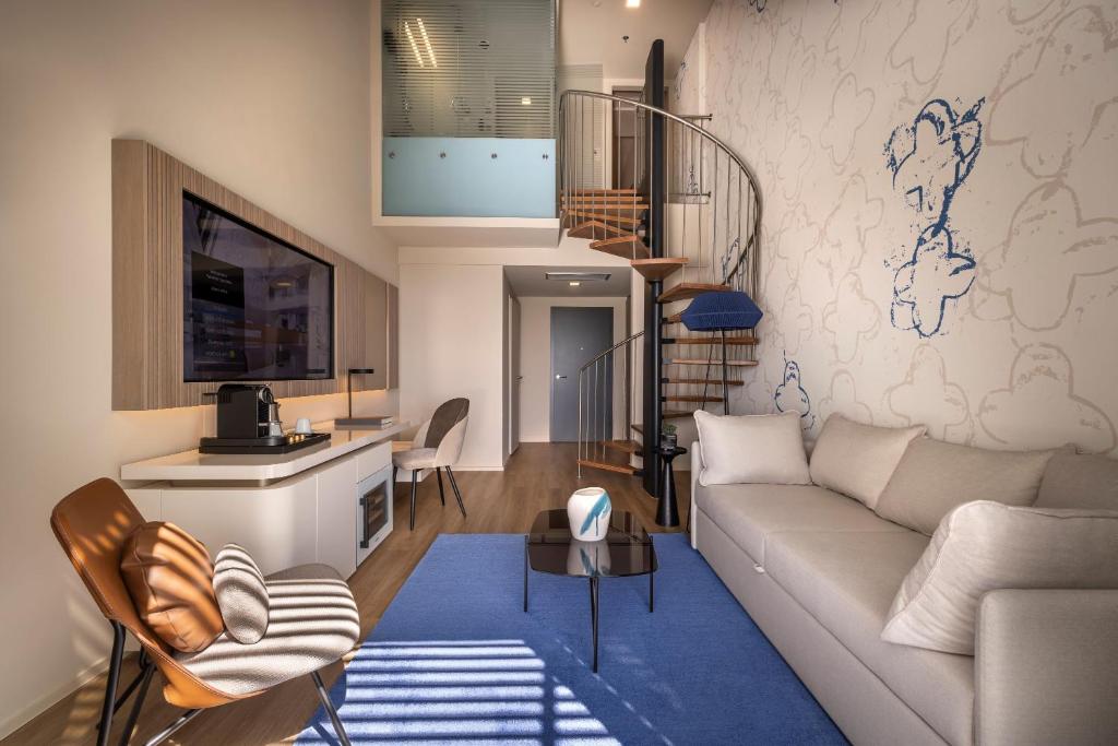 Mūsdienīgs viesistabas dizains ar spirālveida kāpnēm, gaišām krāsām un ērtu dīvānu, kas rada mājīgu atmosfēru. Interjers papildināts ar elegantu televizoru un stilīgu kafijas automātu.