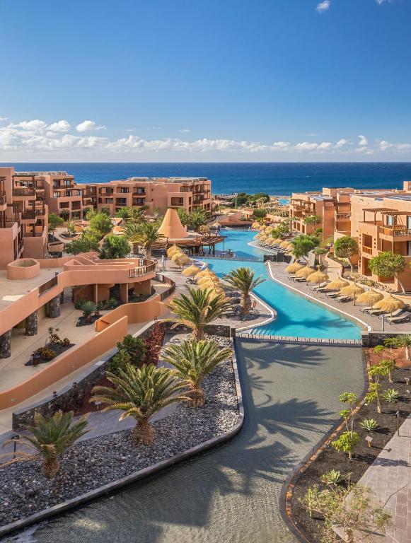 Luksusa kūrorts ar plašu baseinu un palmām, kas atrodas pie jūras. Skaista ainava ar saulainu debesu fonu.