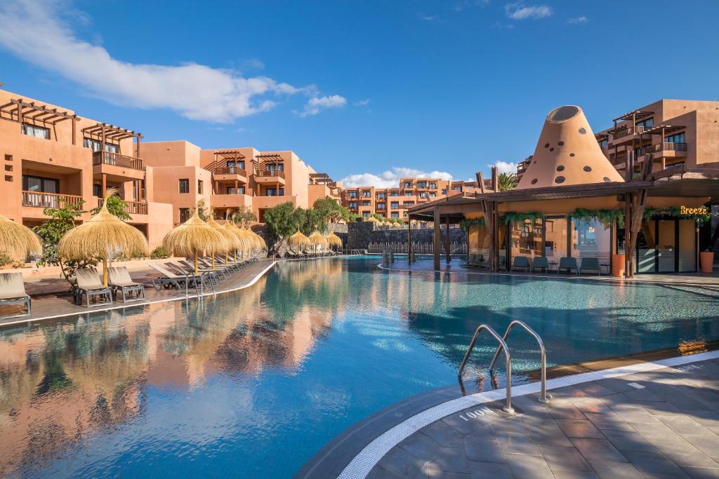 Luksusa kūrorts ar baseinu un palmām, apkārt esošās dzīvojamās ēkas ar siltām krāsām un skaistu debesi. Ideāla vieta atpūtai un relaksācijai.