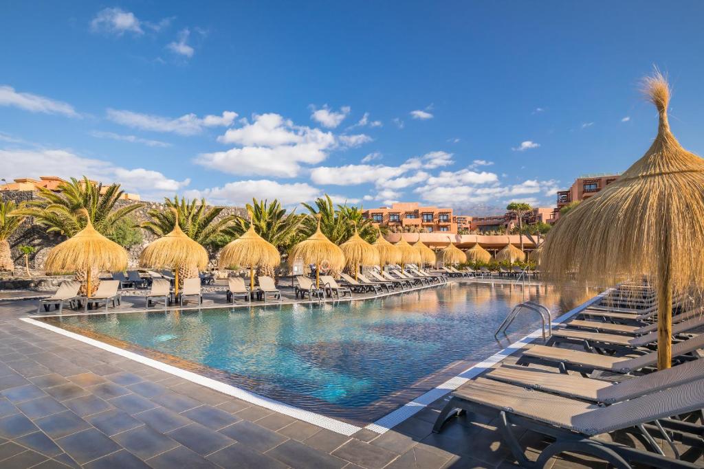 Peldbaseins ar saules lietām un palmām, apkārt ir sauļošanās krēsli un skaidras debesis. Ideāla vieta atpūtai un relaksācijai.