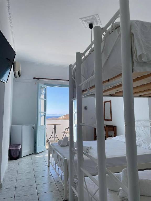 Gaisīga viesnīcas istaba ar divstāvu gultu, atvērtu logu un skatu uz jūru. Telpā ir televizors, ledusskapis un galds ar krēsliem.