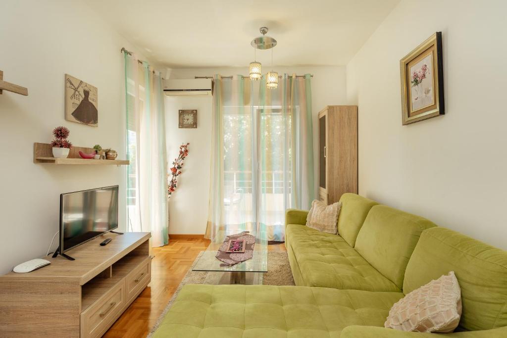 Mūsdienīgs viesistabas interjers ar zaļu dīvānu, koka mēbelēm un gaisīgām aizkariem, radot mājīgu un viesmīlīgu atmosfēru.