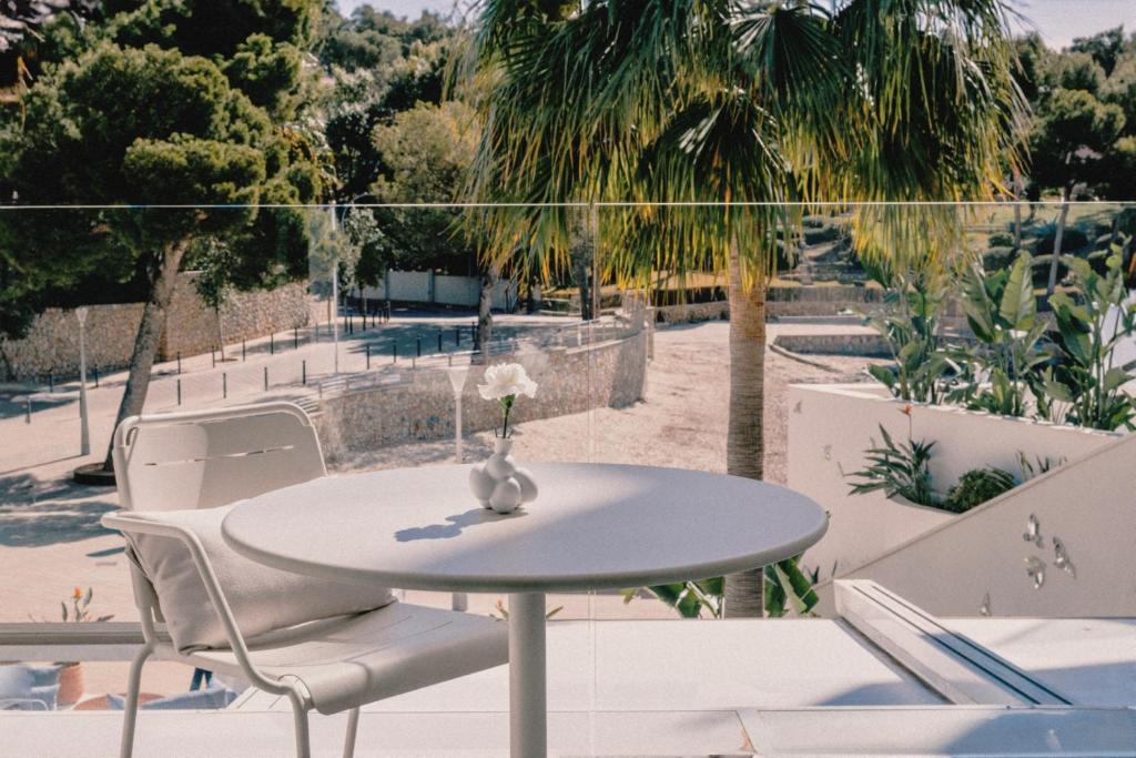 Balta galda un krēsla kompozīcija ar ziedu vāzē, redzama terase ar palmām un zaļumi fona. Ideāla vieta relaksācijai un atpūtai.