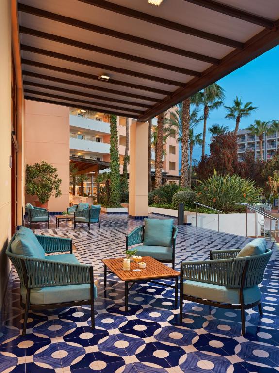 Terase ar zilu un baltu rakstu flīzēm, kurā ir zaļas mēbeles un kaktusi, piedāvā relaksējošu atmosfēru. Apkārt ir palmām un citiem augiem.