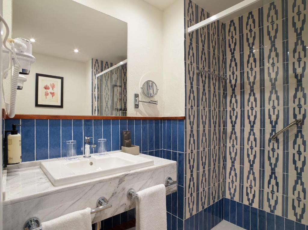 Moderns vannas istabas interjers ar zilu flīžu apdari, baltu izlietni un spoguli. Stilīgu detaļu un praktisku risinājumu kombinācija.