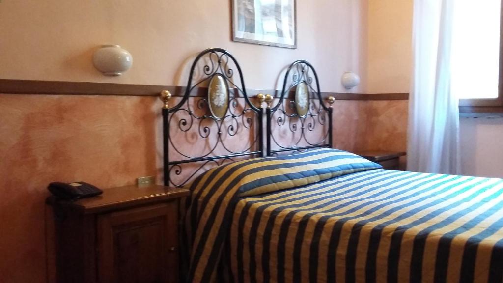 Gultas istaba ar dzelzs gultu, svītrotu gultasveļu un koka naktsgaldiņu. Telpā ir gaisma un logs ar aizkaru, radot mājīgu atmosfēru.