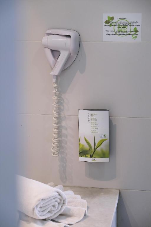 Fēnu žāvētājs un higiēnas produkti vannas istabā, uz balta flīžu fona. Dekorācija ar zaļām lapām.