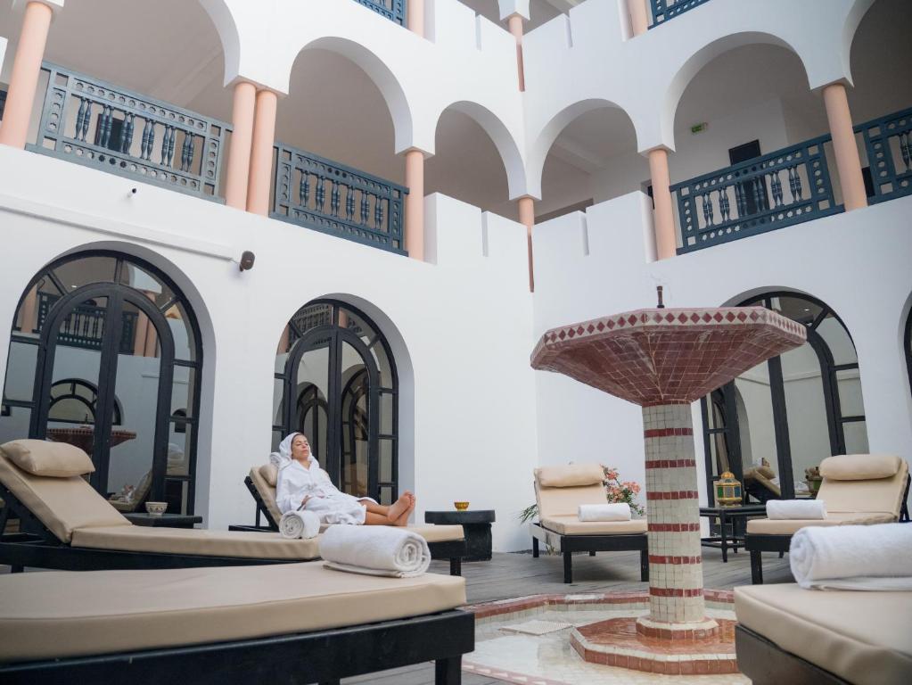 Spa atklātā telpa ar relaksējošiem guļamkrēsliem un strūklaku, kur sieviete atpūšas. Mierīga atmosfēra un eleganta arhitektūra veido ideālu vietu atpūtai.