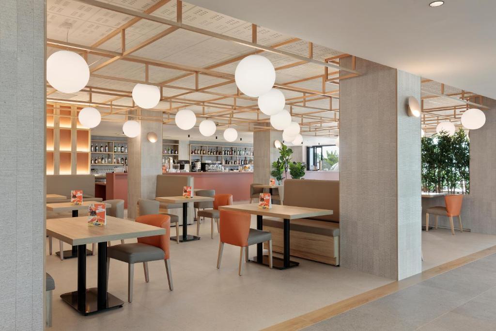 Mūsdienīgs restorāna interjers ar gaisīgu dizainu, apaļām lampām un koka akcentiem, kas rada patīkamu atmosfēru. Galdi un krēsli ir izvietoti ērtai sanākšanai.