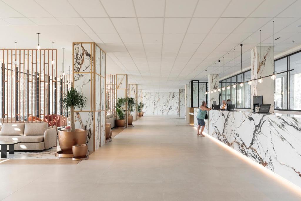 Mūsdienīgs viesnīcas reģistratūras interjers ar marmora sienām un stilīgu mēbeļu izvietojumu. Gaismas elementu kombinācija un zaļie augi rada patīkamu atmosfēru.